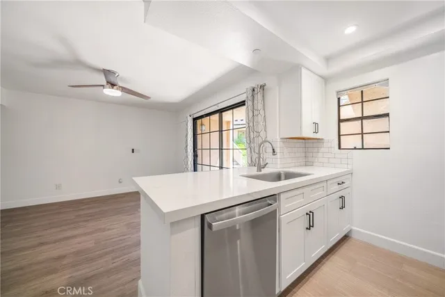 a kitchen with a sink dishwasher and white cabinets with wooden floor