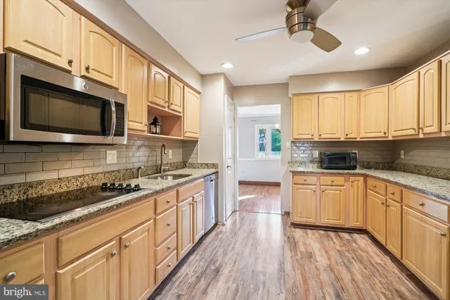 a kitchen with stainless steel appliances granite countertop wooden cabinets a stove top oven a sink and dishwasher with wooden floor