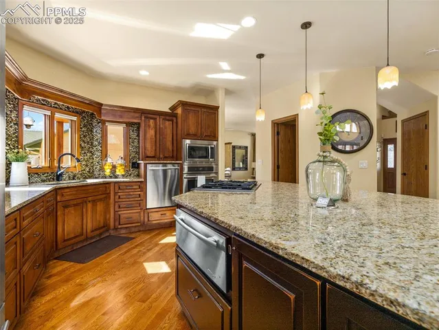 a kitchen with stainless steel appliances granite countertop a sink a stove and a wooden floors