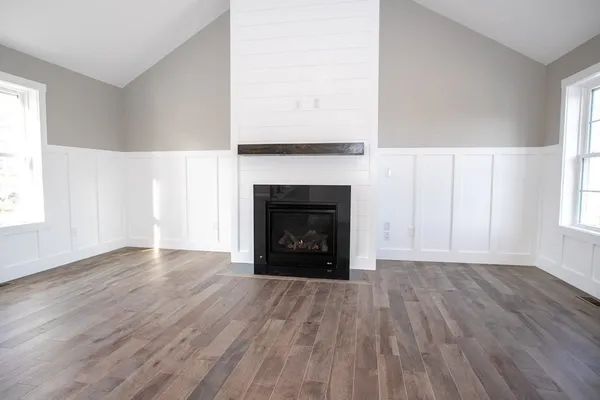 a view of an empty room with wooden floor fireplace and a window