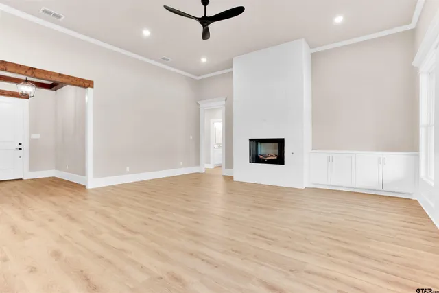 a view of an empty room with wooden floor and a ceiling fan