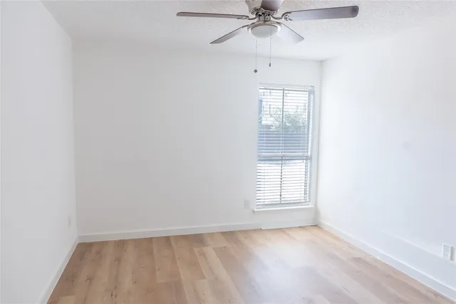 an empty room with wooden floor fan and windows
