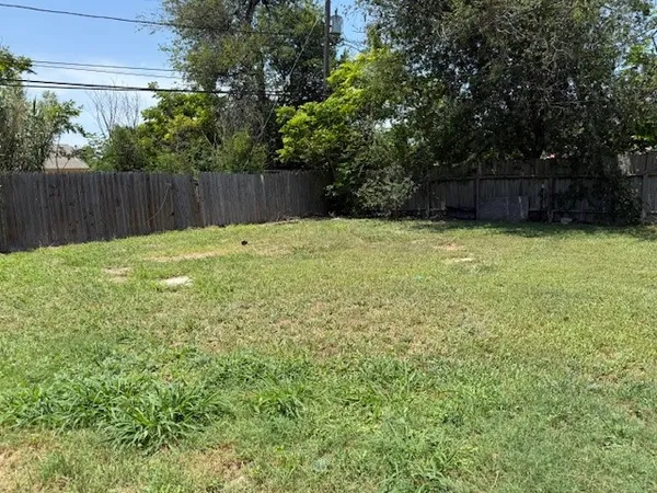 a view of a backyard with large trees and wooden fence