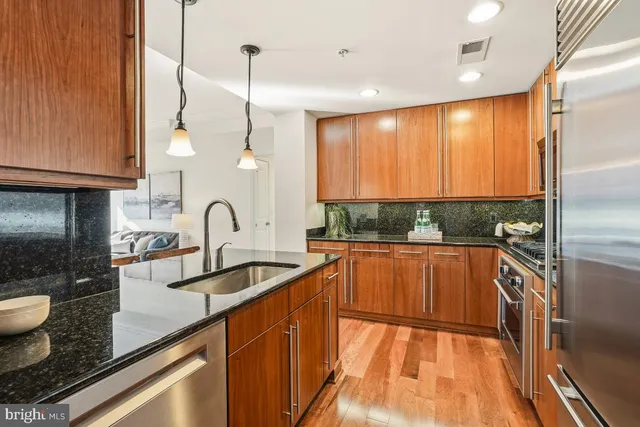 a kitchen with stainless steel appliances granite countertop a refrigerator a stove and a sink with wooden floor