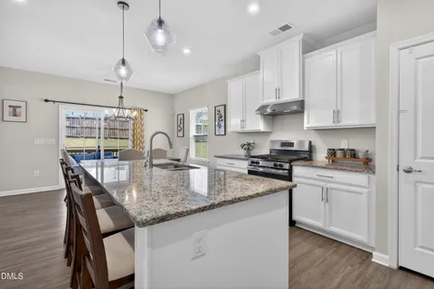 a kitchen with kitchen island granite countertop a stove a sink a dining table and chairs with wooden floor