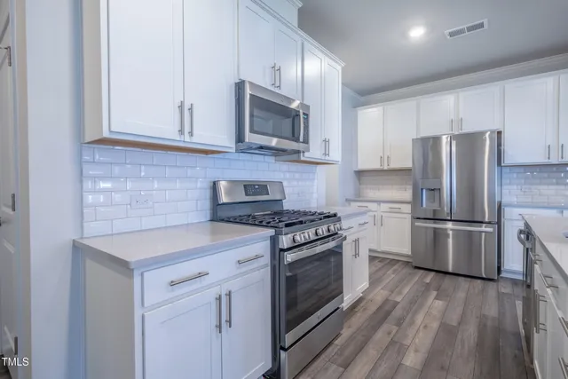 a kitchen with white cabinets stainless steel appliances and wooden floor