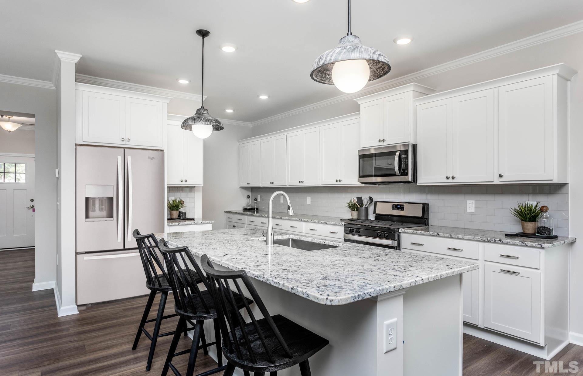 5839 Agrinio Way Raleigh, NC 27603 - Photo 13 of 20 a kitchen with stainless steel appliances kitchen island granite countertop a dining table chairs refrigerator and microwave
