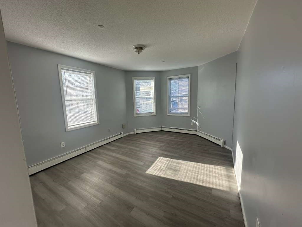 27 Willow Street, Unit A Lawrence, MA 01841 - Photo 4 of 29 an empty room with wooden floor and windows