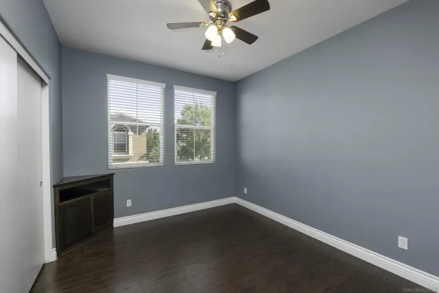 an empty room with wooden floor fan and windows