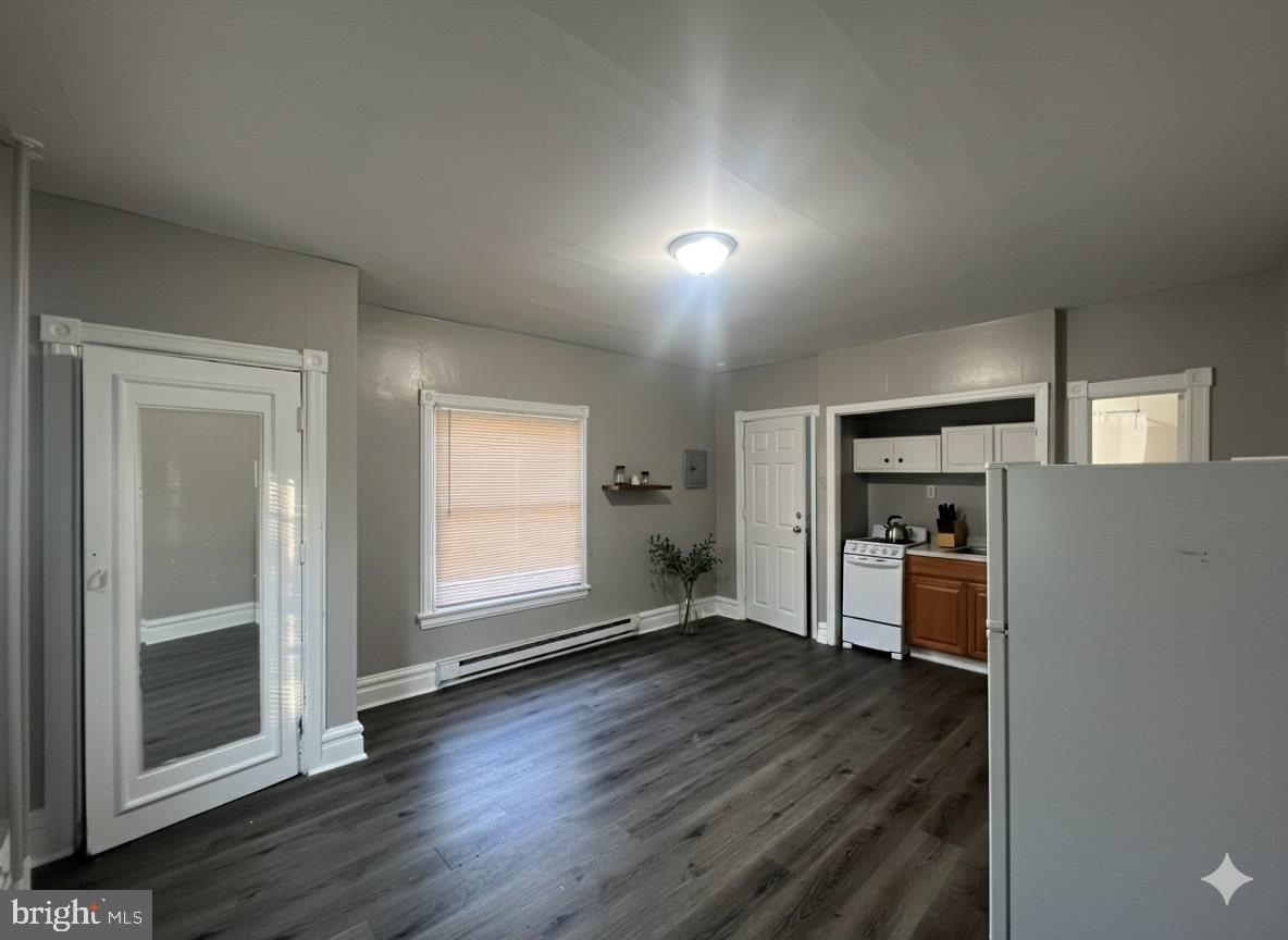 an empty room with wooden floor kitchen view and windows