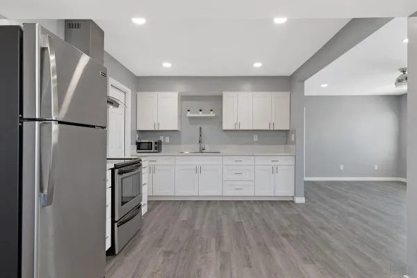 a kitchen with granite countertop a refrigerator stove and white cabinets with wooden floor
