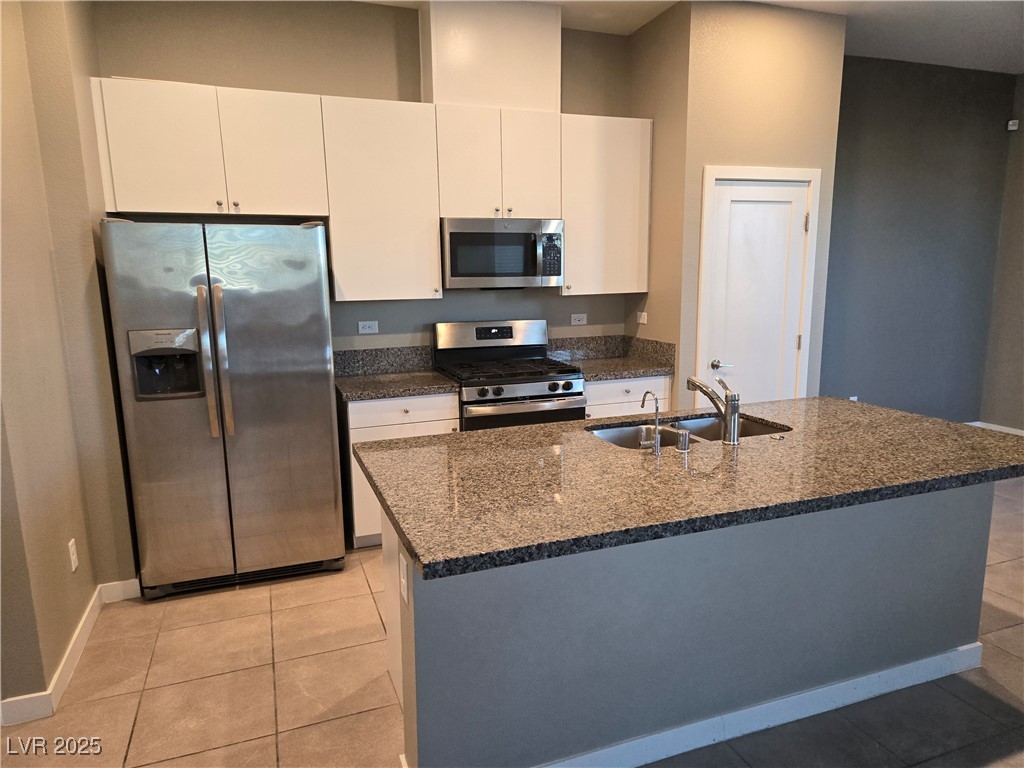 3192 Timorasso Avenue Henderson, NV 89044 - Photo 3 of 16 Kitchen featuring appliances with stainless steel finishes, light tile patterned flooring, dark stone counters, an island with sink, and white cabinetry