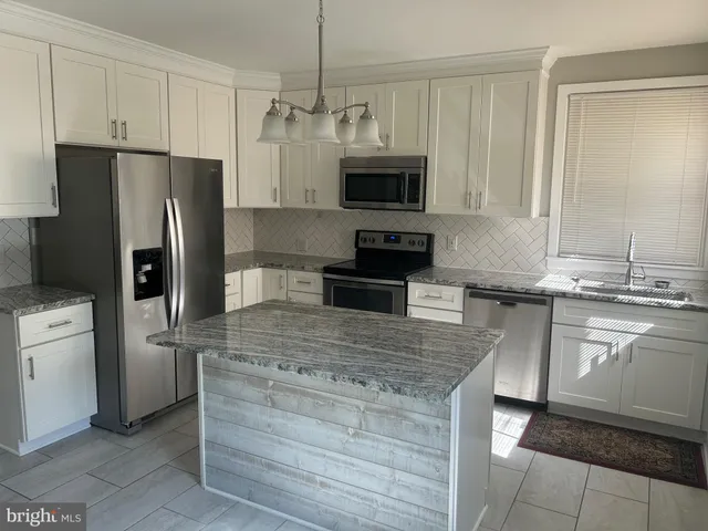 a kitchen with kitchen island granite countertop a refrigerator oven a sink dishwasher and white cabinets with wooden floor