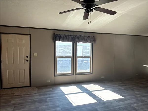 an empty room with wooden floor fan and windows