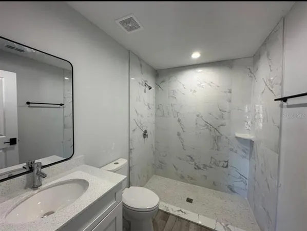 a bathroom with a shower sink vanity mirror and toilet