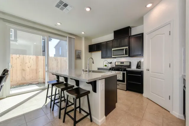 a kitchen with stainless steel appliances granite countertop a stove top oven a sink dishwasher a dining table and chairs with wooden floor