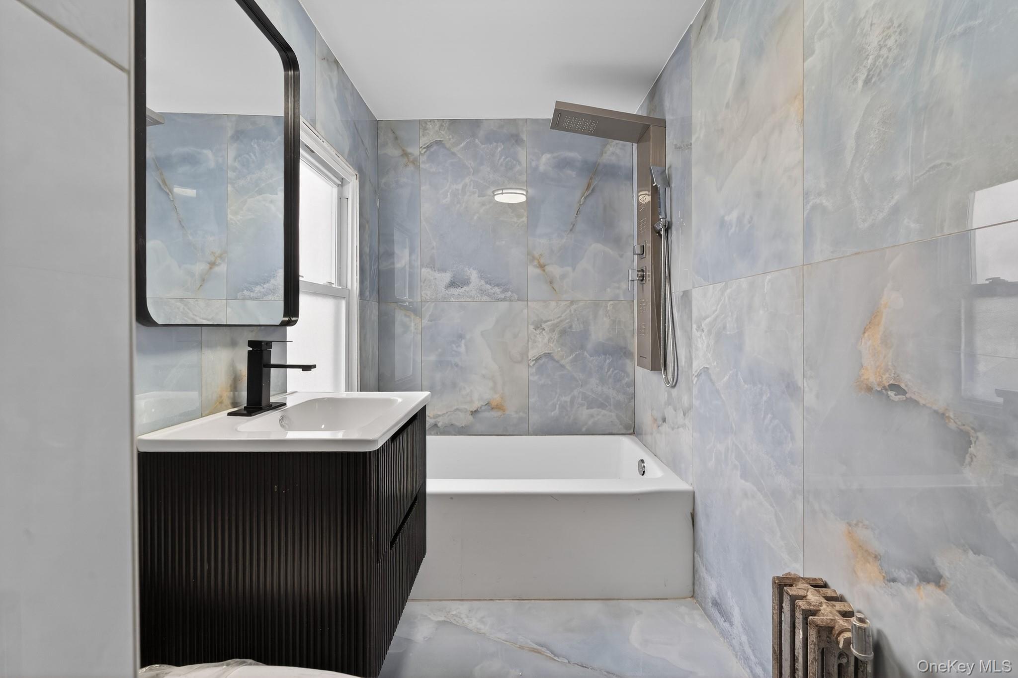 136-03 220th Street Queens, NY 11413 - Photo 9 of 27 a bathroom with a sink a mirror and a bathtub