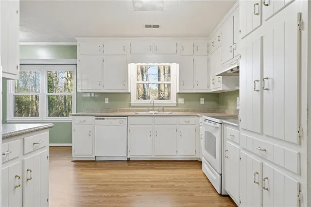 a kitchen with granite countertop white cabinets white appliances a sink and a window