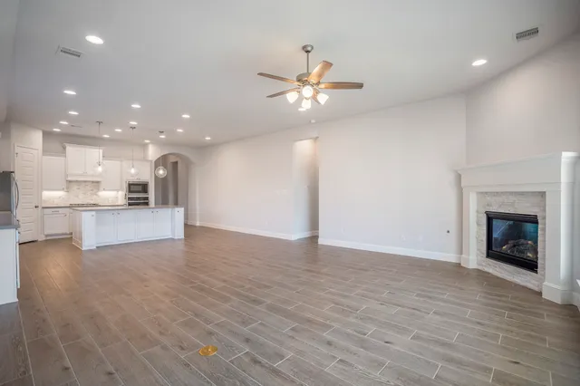 a view of an empty room and kitchen with fireplace ceiling fan