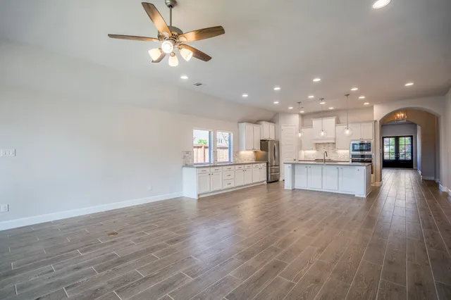 a view of an empty room and kitchen with wooden floor
