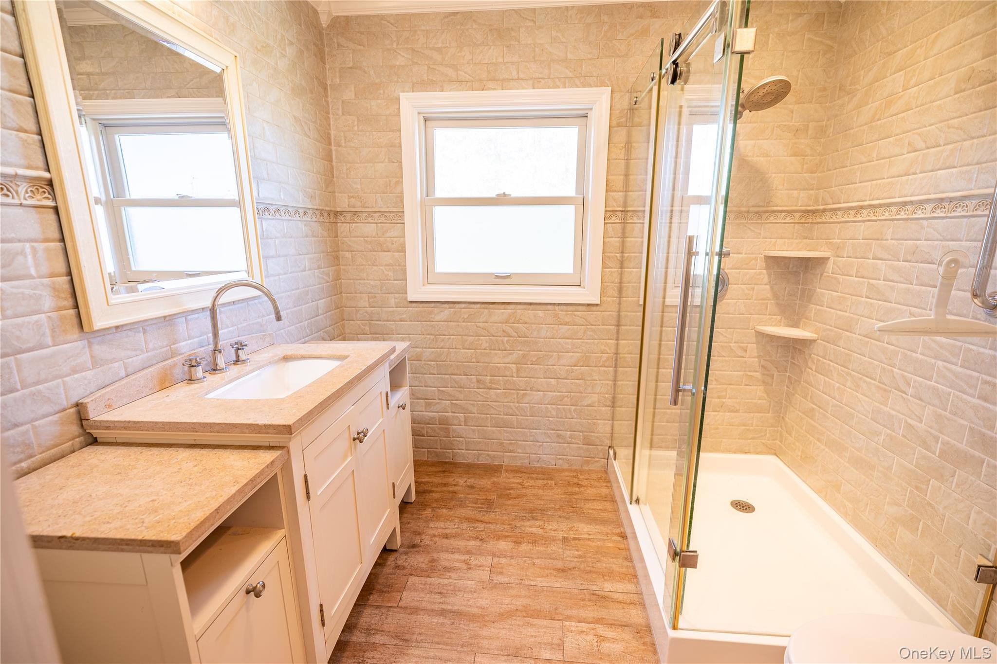 84 Rhoda Avenue North Babylon, NY 11703 - Photo 11 of 23 The bathroom features a vanity with a light-colored countertop and a rectangular sink, a large mirror, and a window providing natural light