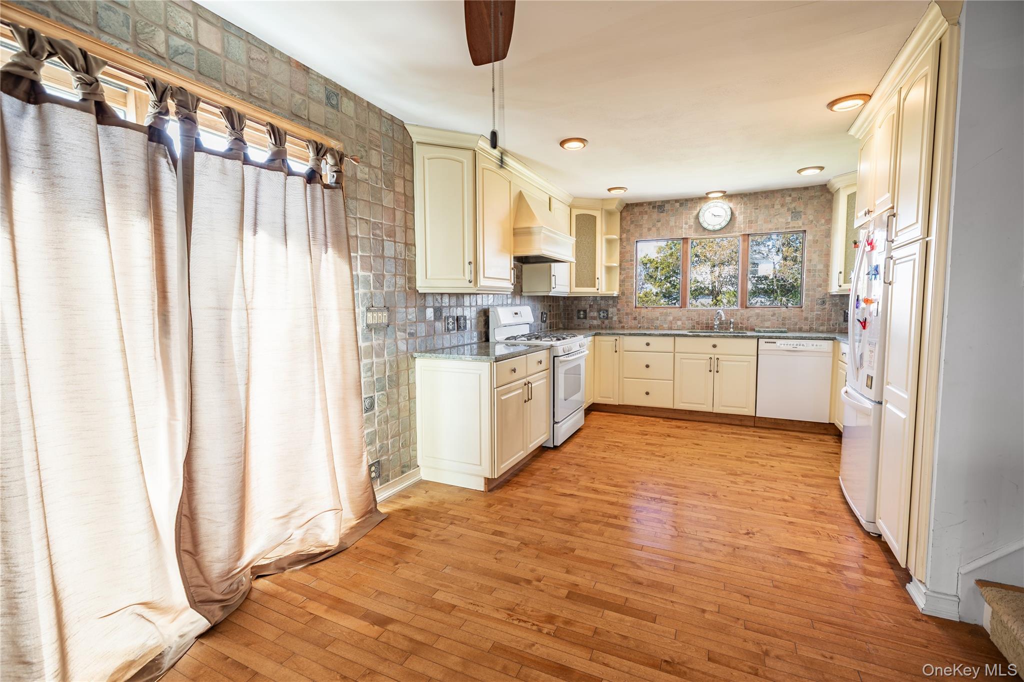 84 Rhoda Avenue North Babylon, NY 11703 - Photo 6 of 23 Spacious kitchen featuring wood flooring, cream cabinetry, white appliances, and a tiled backsplash