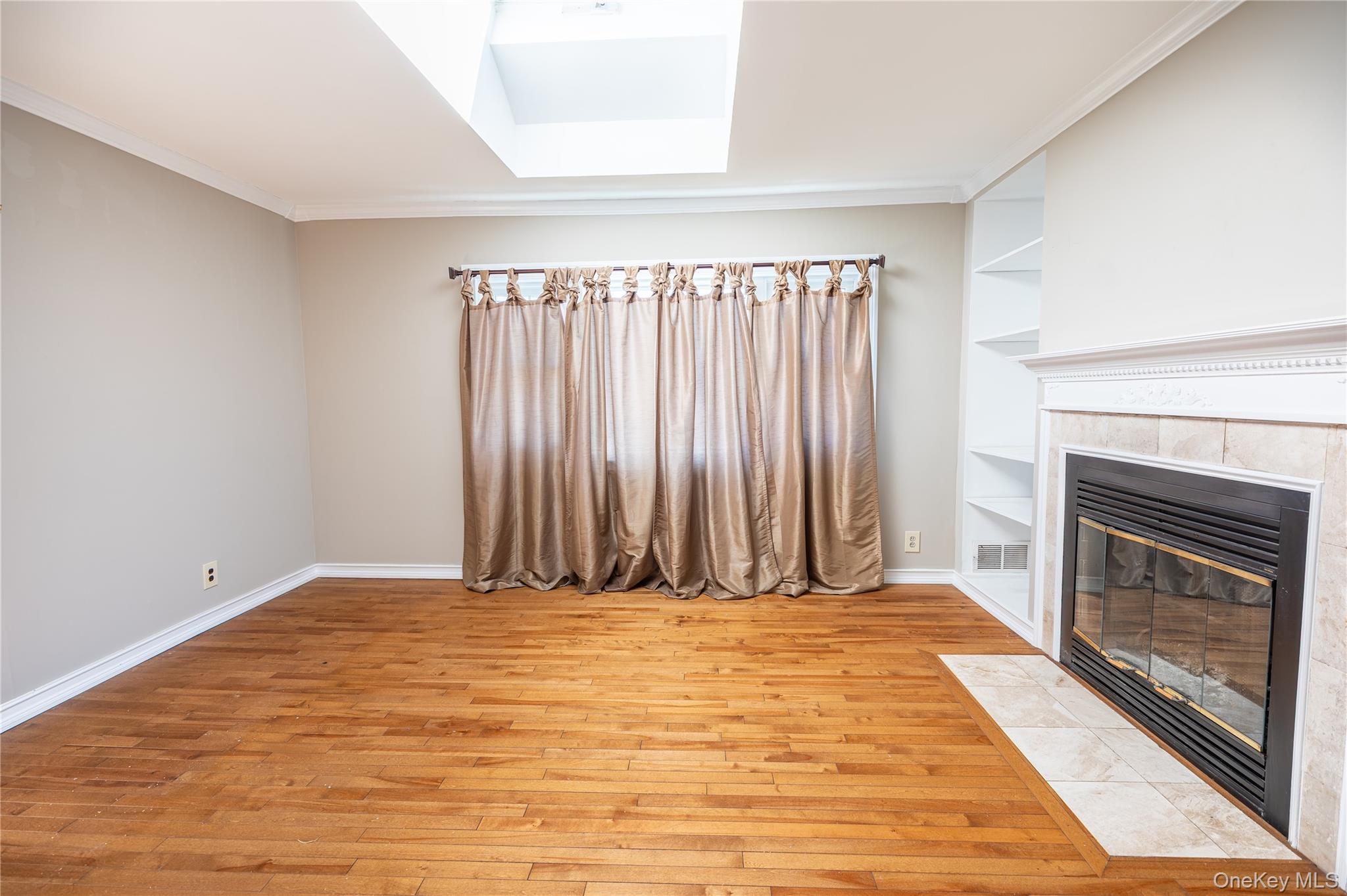 84 Rhoda Avenue North Babylon, NY 11703 - Photo 9 of 23 Living area featuring hardwood floors, a gas fireplace with a tiled surround and mantelpiece, built-in shelving, and a skylight