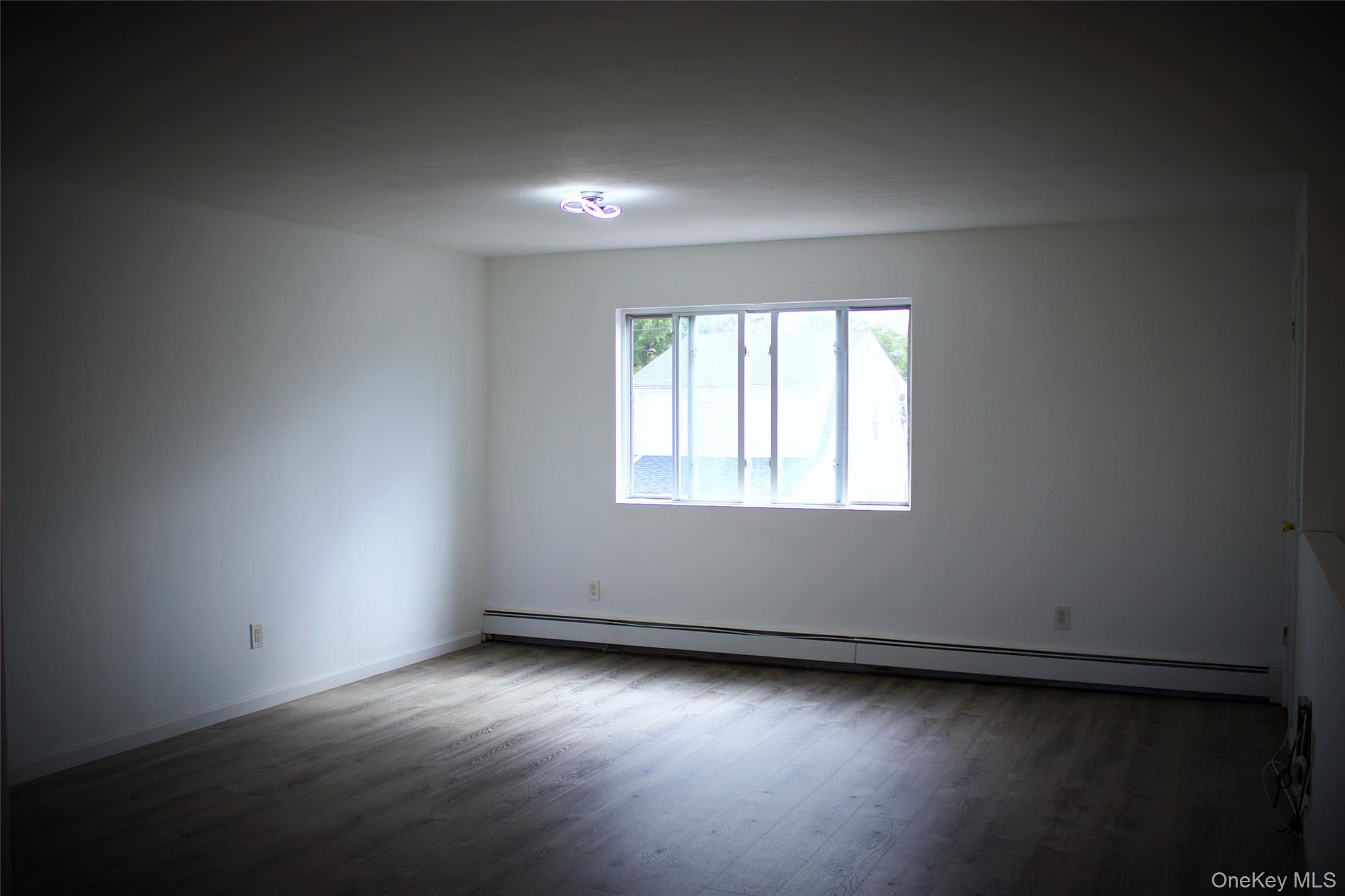 174-27 126th Avenue, Unit 2 Queens, NY 11434 - Photo 4 of 12 an empty room with wooden floor and windows