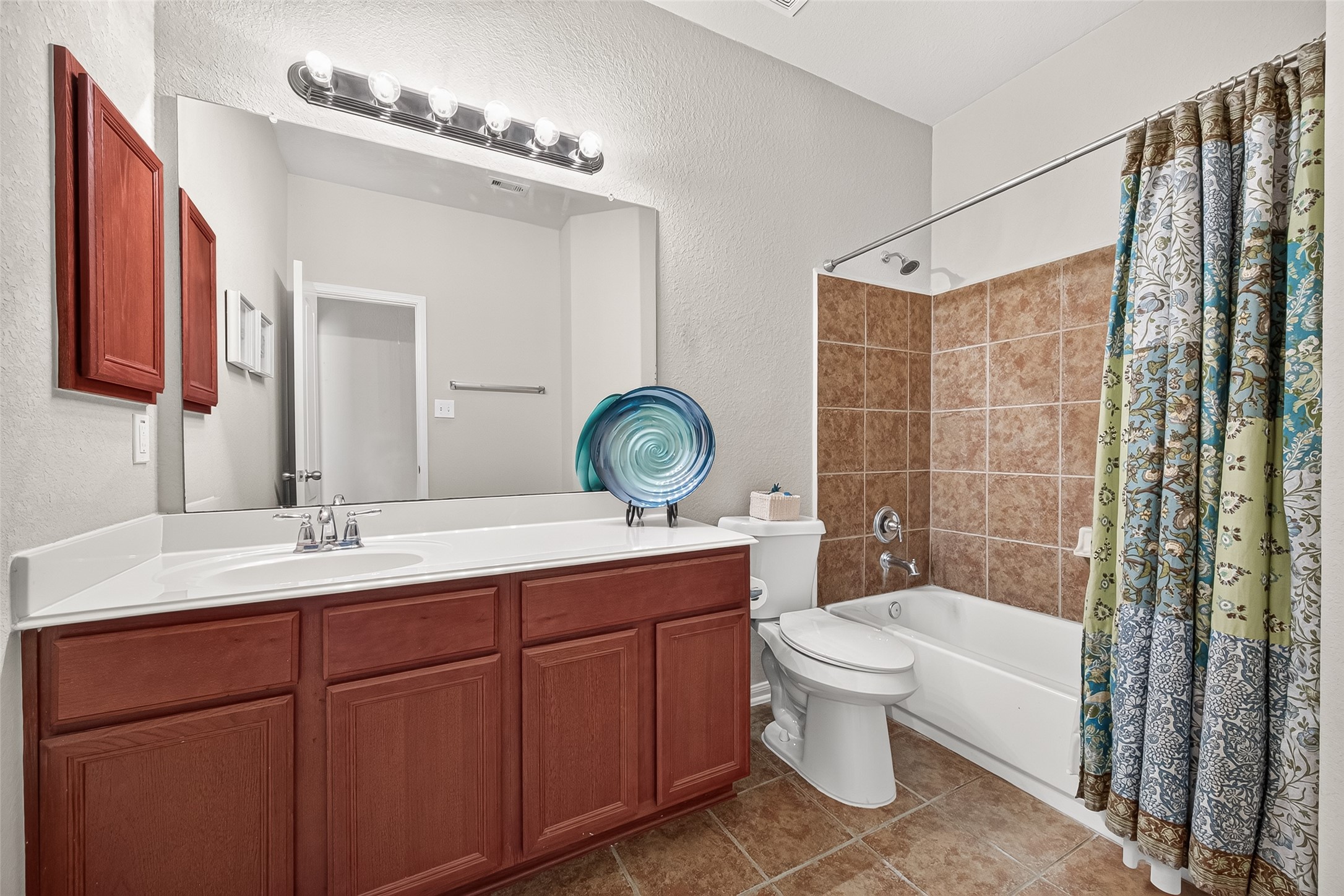 4910 Culver Lane Rosenberg, TX 77471 - Photo 19 of 50 The guest bathroom features a spacious vanity with rich wood cabinets, a large mirror with bright lighting, tiled flooring, and a shower-tub combination.