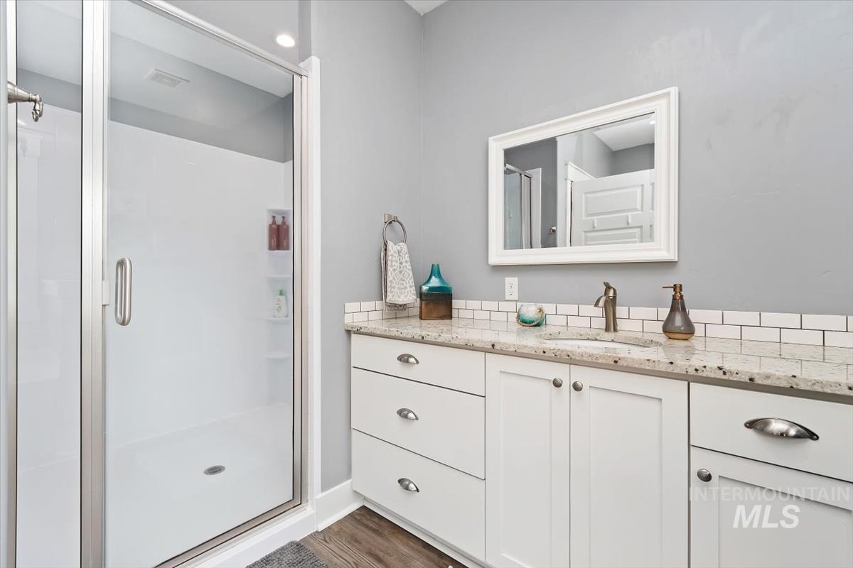 15015 Leon Lane Caldwell, ID 83607 - Photo 22 of 44 Bathroom featuring a glass-enclosed shower, white subway tile backsplash, white vanity cabinetry with brushed nickel hardware, and a stone-finish countertop