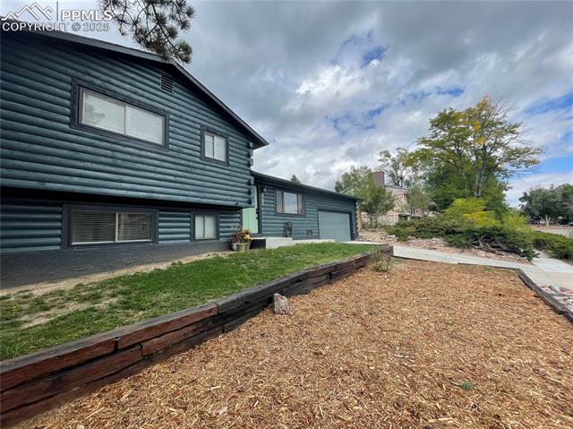 Rear view of property with an attached garage, driveway, and faux log siding