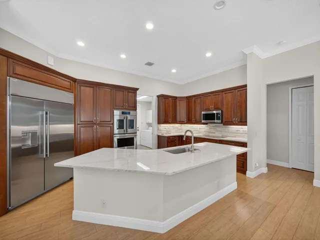 a large white kitchen with stainless steel appliances kitchen island a stove a refrigerator a sink dishwasher and a refrigerator with wooden floor