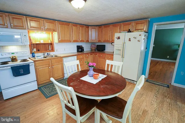 a kitchen with stainless steel appliances granite countertop a stove a refrigerator a sink a dining table and chairs with wooden floor