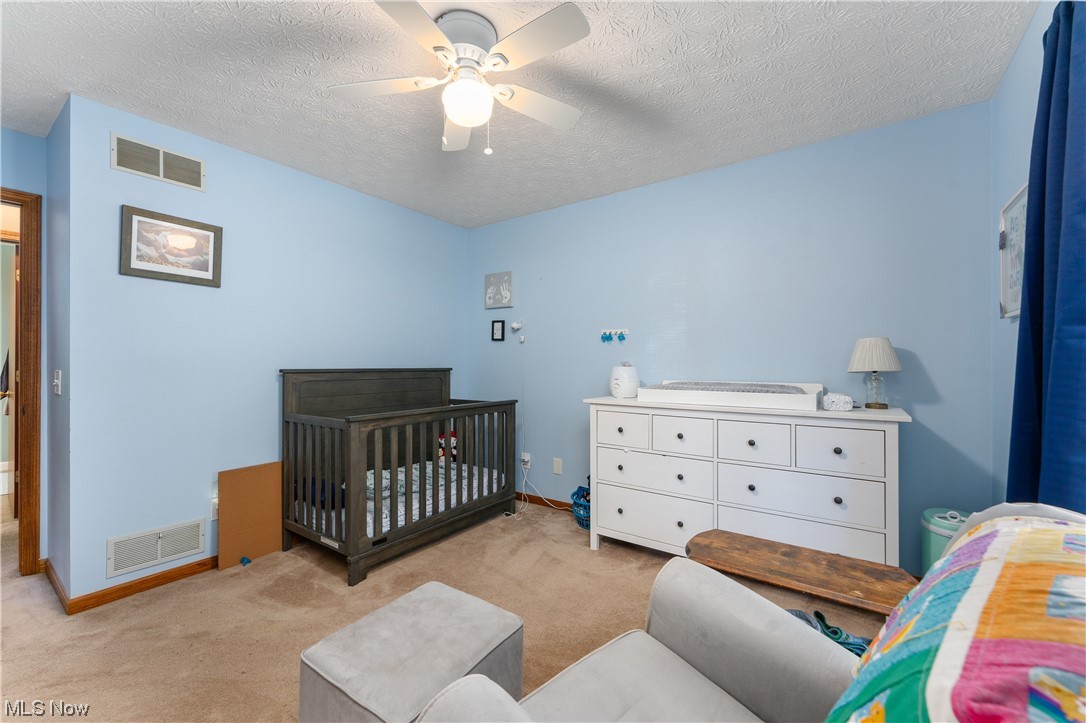 5226 Johnnycake Ridge Northeast Canton, OH 44705 - Photo 22 of 32 Bedroom featuring a textured ceiling, ceiling fan, light colored carpet, and a nursery area