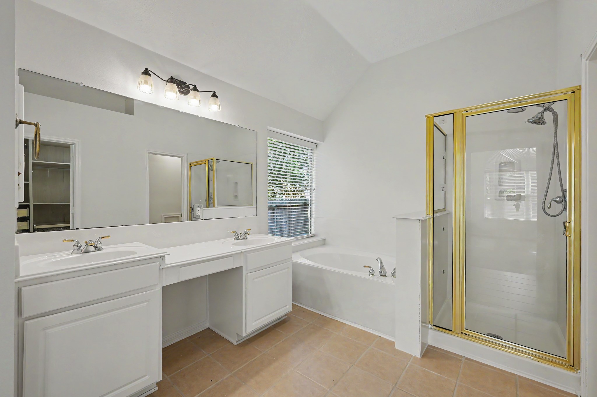 14 South Rambling Ridge Place The Woodlands, TX 77385 - Photo 21 of 42 Spacious primary bath offers dual vanities with a dedicated makeup area, a relaxing soaking tub, separate glass-enclosed shower, abundant natural light, and a vaulted ceiling for an open, airy feel.