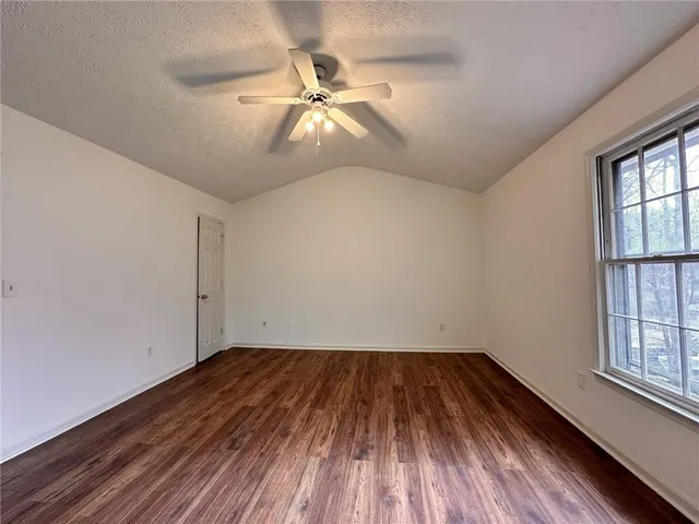 an empty room with wooden floor fan and windows