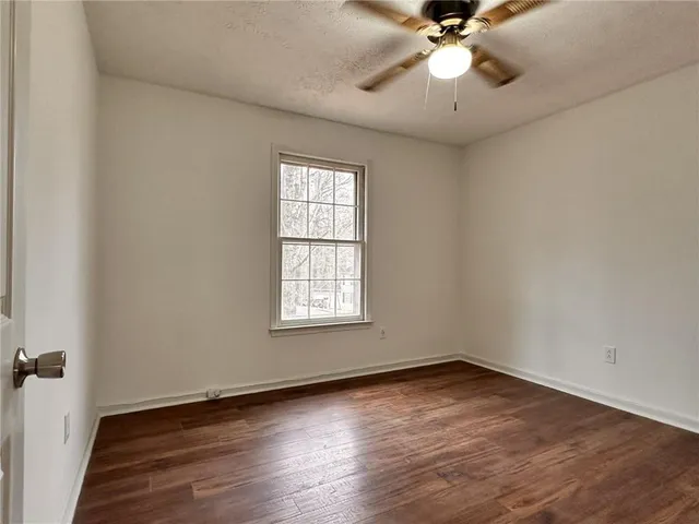 an empty room with wooden floor fan and windows