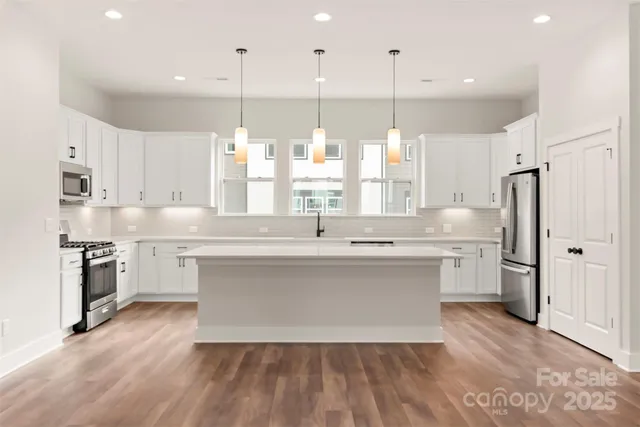 a kitchen with stainless steel appliances granite countertop a sink a refrigerator and a wooden floor