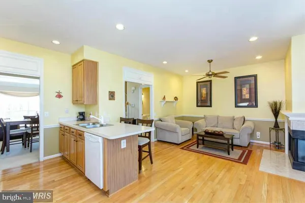 a living room with stainless steel appliances kitchen island granite countertop a sink dishwasher a dining table and chairs with wooden floor