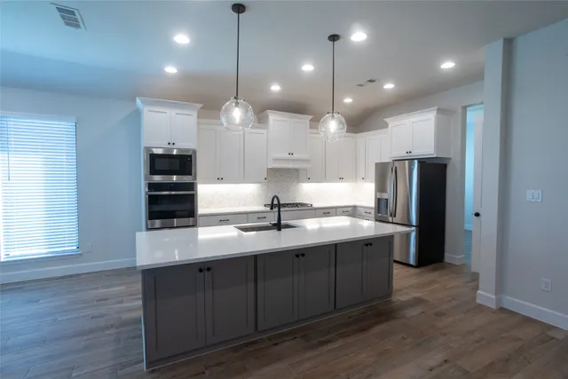 a kitchen with stainless steel appliances granite countertop a sink a refrigerator and a stove with wooden floor