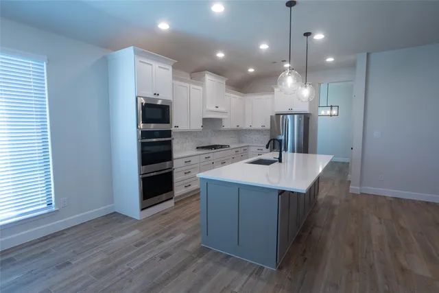 a kitchen with kitchen island a sink stainless steel appliances and wooden floor