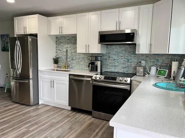 a kitchen with granite countertop a refrigerator oven a sink dishwasher and white cabinets with wooden floor