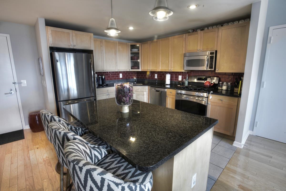 700 Grove Street, Unit 12J Jersey City, NJ 07310 - Photo 3 of 16 a kitchen with granite countertop a table chairs microwave and refrigerator
