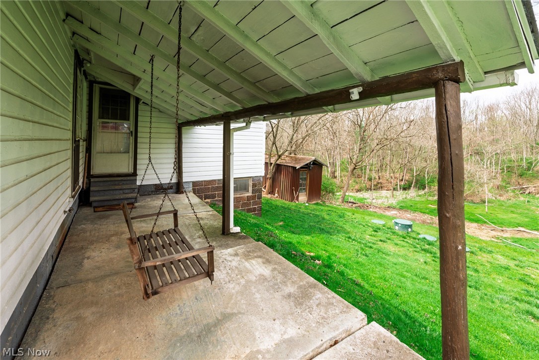 1069 West Nimisila Road New Franklin, OH 44216 - Photo 19 of 26 The property features a covered porch with a wooden swing, offering views of a grassy area and wooded surroundings