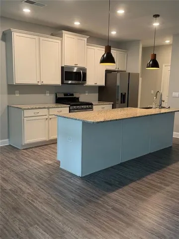a large kitchen with stainless steel appliances granite countertop a sink a stove a microwave a refrigerator and white cabinets with wooden floor