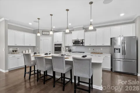a kitchen with stainless steel appliances granite countertop a dining table chairs refrigerator and microwave