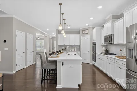 a kitchen with stainless steel appliances kitchen island granite countertop a sink a stove a refrigerator cabinets and a dining table with wooden floor