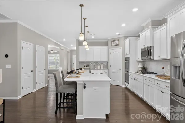 a kitchen with stainless steel appliances kitchen island granite countertop a sink a stove a refrigerator cabinets and a dining table with wooden floor