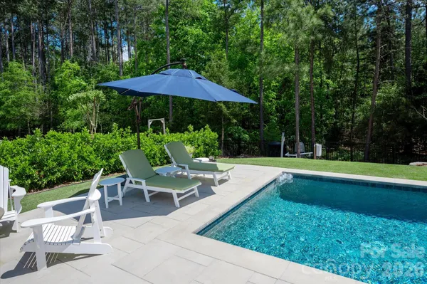 a view of pool with lawn chairs under an umbrella