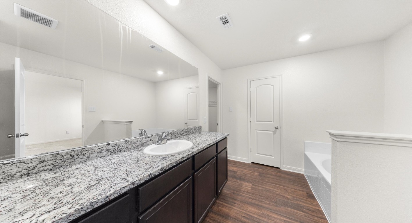 18524 Speculator Lane Elgin, TX 78621 - Photo 21 of 34 Full bath featuring a garden tub, vanity, dark wood-type flooring, and recessed lighting